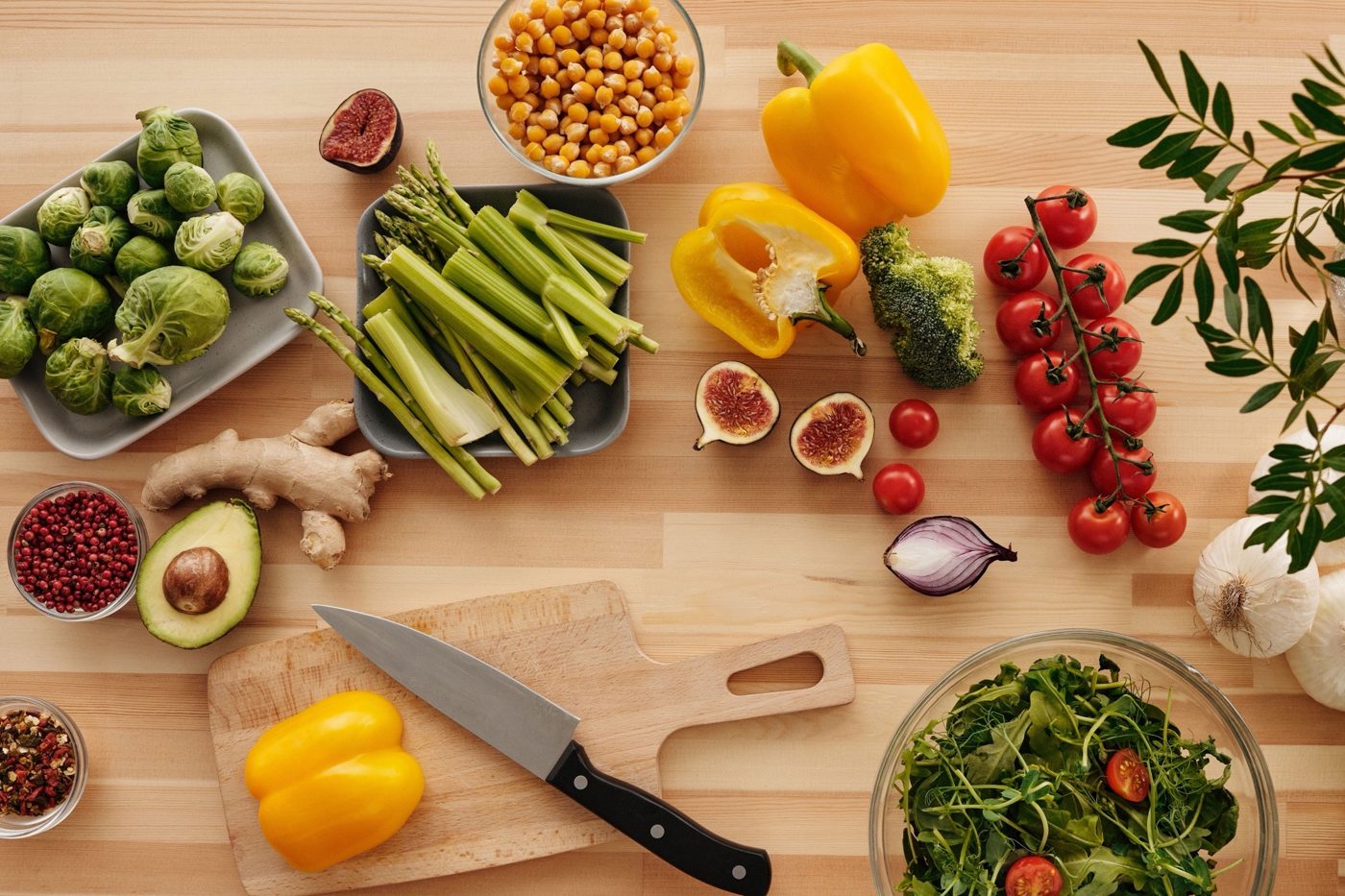 Fresh vegetables, herbs and a salad bowl laid out on a wooden counter ready for meal prep